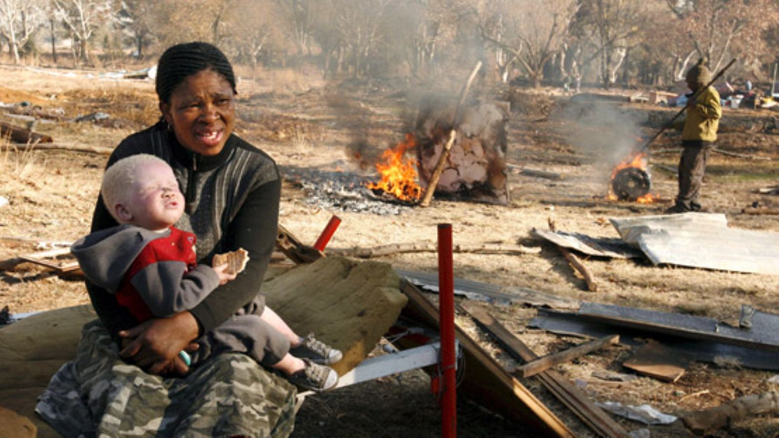 A mother holds her albino daughter to try to keep warm in what remains of her house that was demolished after the squatter community they lived with where evicted from land owned by a mining house, Johannesburg, South Africa, 27 June 2007.