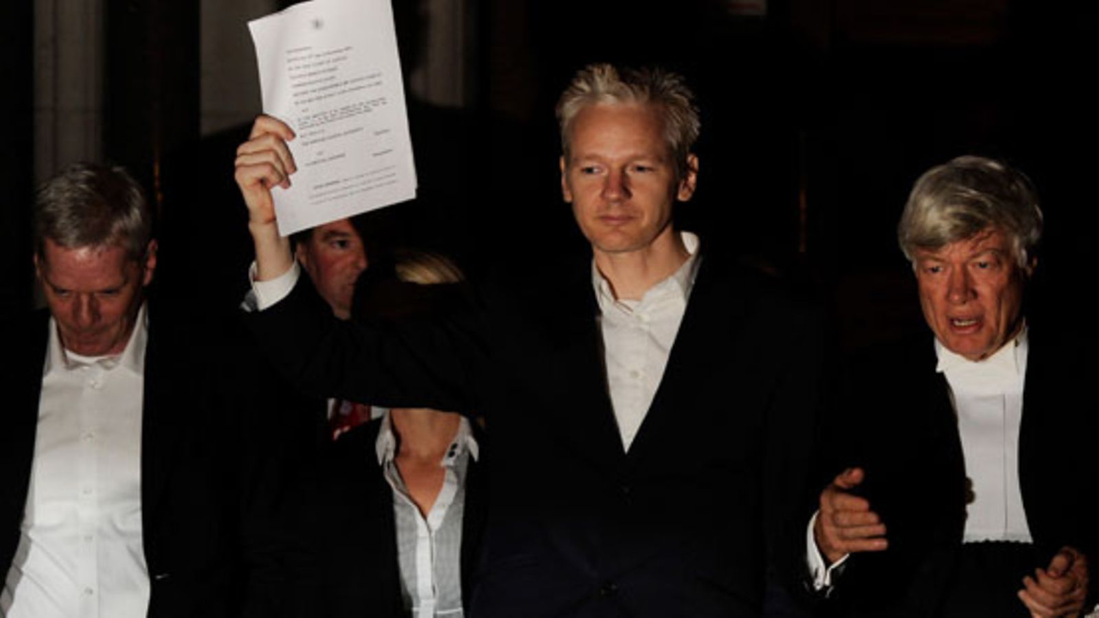 Julian Assange näyttää tiedostusvälineille Lontoon ylioikeuden laatimaa asiakirjapaperia 16.12., jossa hänet vapautetaan takuita vastaan.