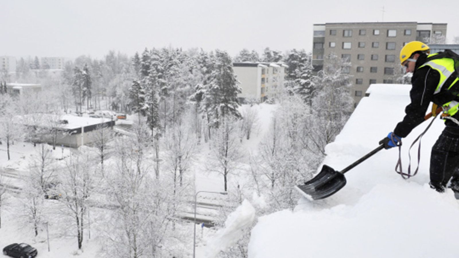 Työnjohtaja Kari Ruusukunnas lapion varressa pudottamassa lunta kerrostalon katolla Espoon Matinkylässä 20. tammikuuta 2011. || Snow dropping from the roof in Espoo, Finland 21 Janyary 2010.  Lehtikuva.