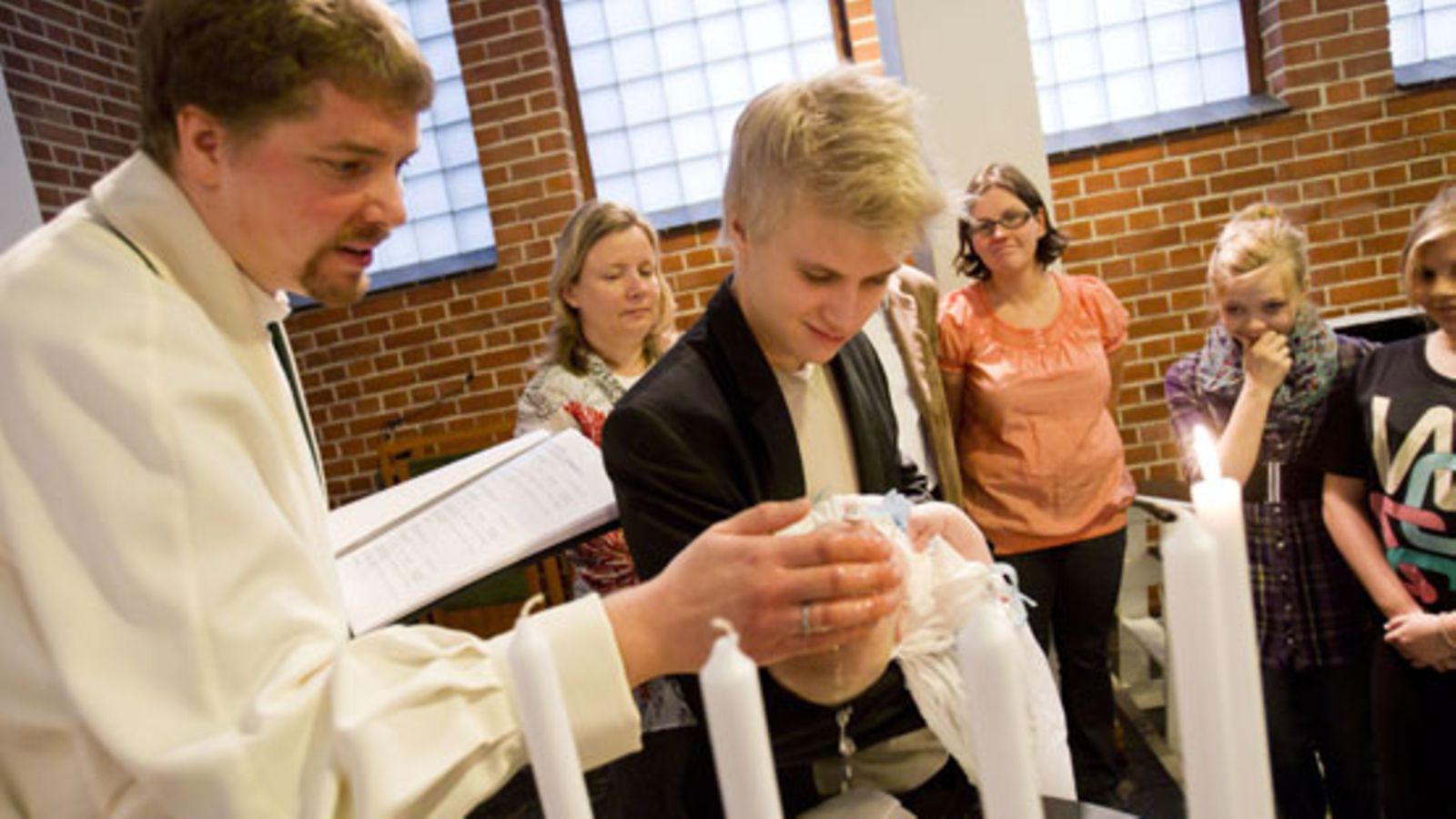 Pastori Toni Fagerholm kastaa Akseli-kummin pitelemän Sampo-vauvan Tikkurilan kirkossa Vantaalla 31. lokakuuta 2010, Sampon äiti Marita Anttila (oik.) seuraa toimitusta taustalla. Vantaan seurakunnat järjestivät kirkoissaan yhteiskastetilaisuuden sunnuntaina.