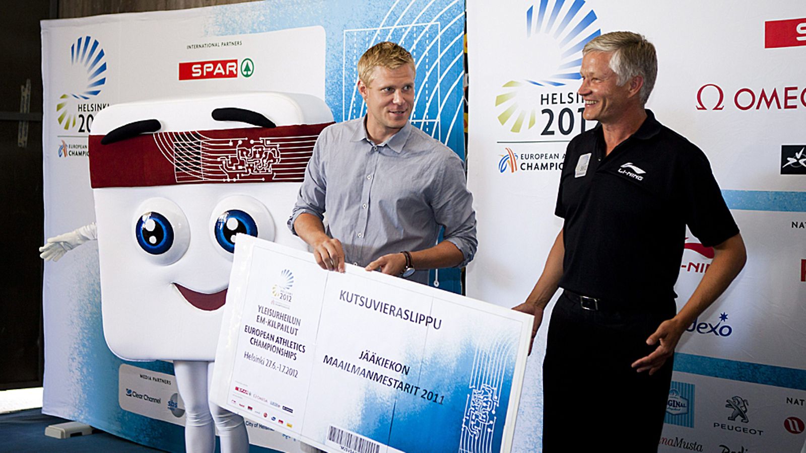EM2012 järjestelytoimikunnan puheenjohtaja Antti Pihlakoski antaa MM-jääkiekkojoukkoeen kutsuvieras lipun Mikko Koivulle vierellä Helsingin EM-kisojen kisamaskotti Appy