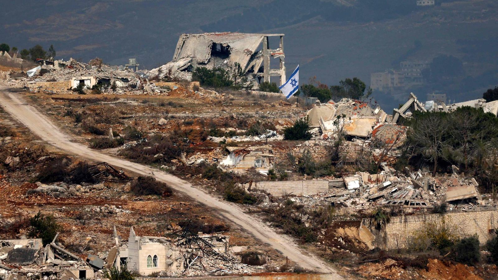 Israelin pohjoisrajalta otetussa kuvassa näkyy Israelin lippu keskellä Israelin pommitusten aiheuttamaa tuhoa Etelä-Libanonin Odaissehin kylässä 4. joulukuuta 2024.