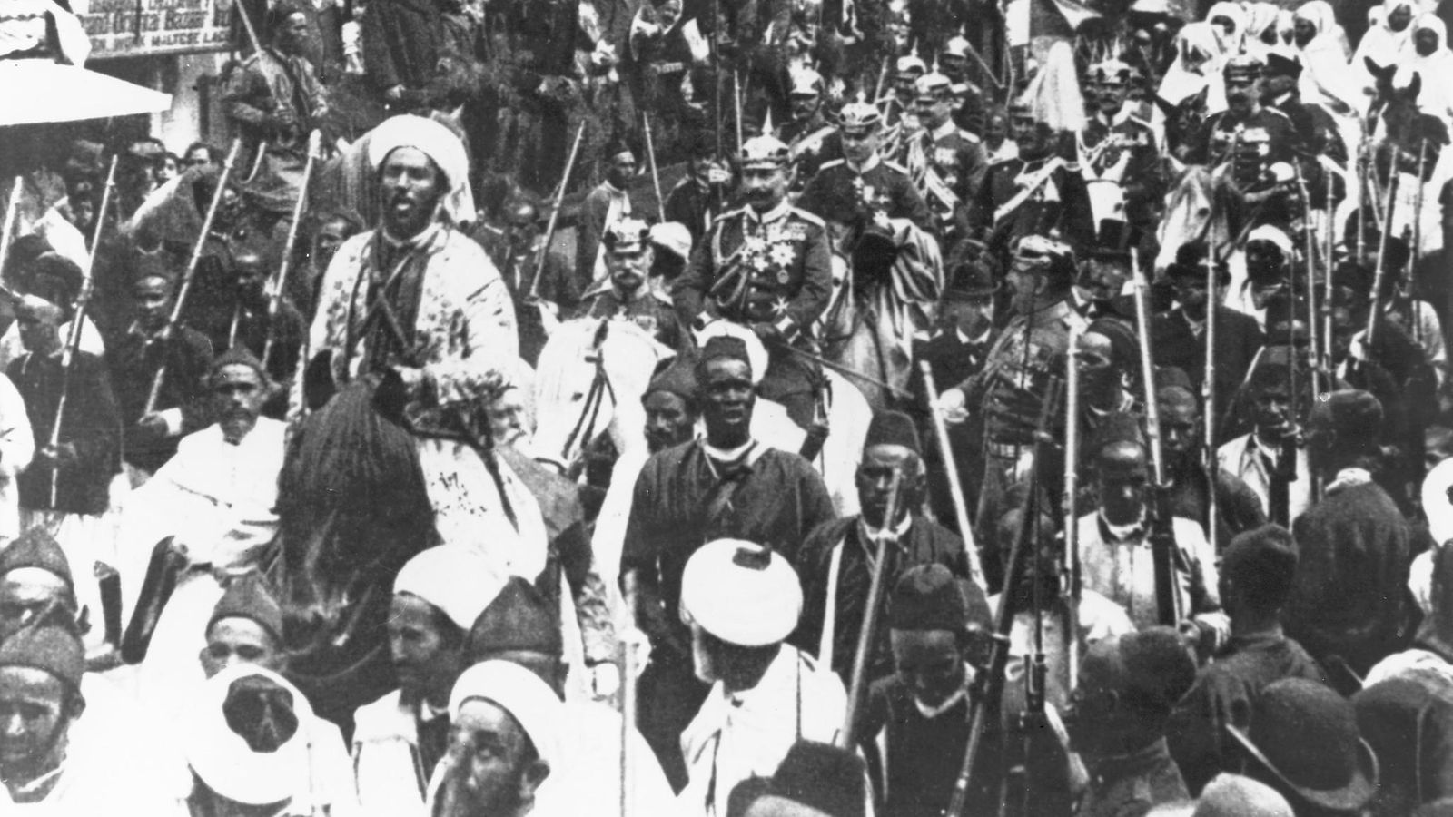 Mustavalkoisessa valokuvassa paraatiasuun pukeutunut Saksan keisari Wilhelm II ratsastaa saattueineen väkijoukon keskellä.