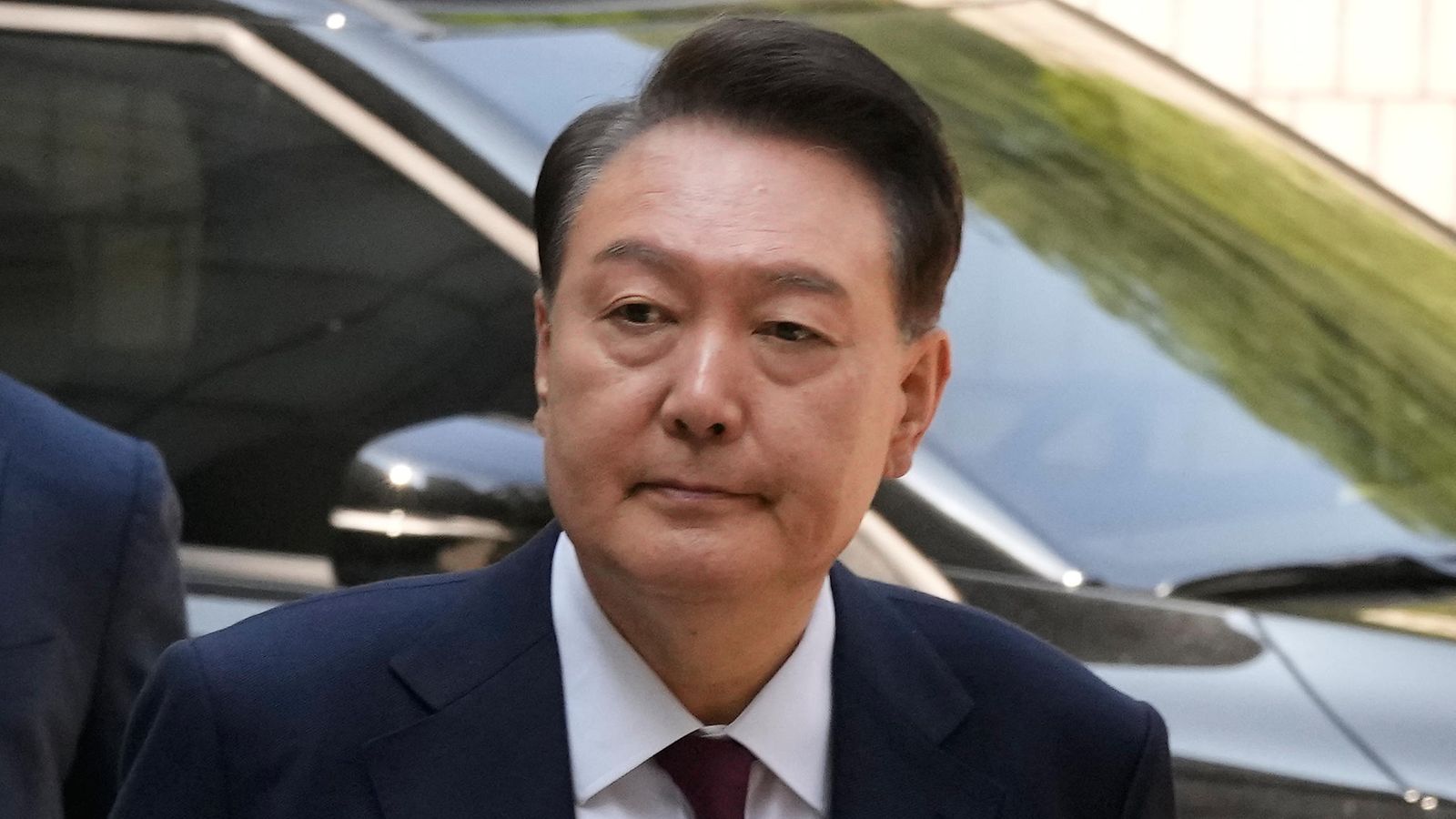 Tummaan pukuun sonustautunut Yoon Suk-yeol kävelee autolta.