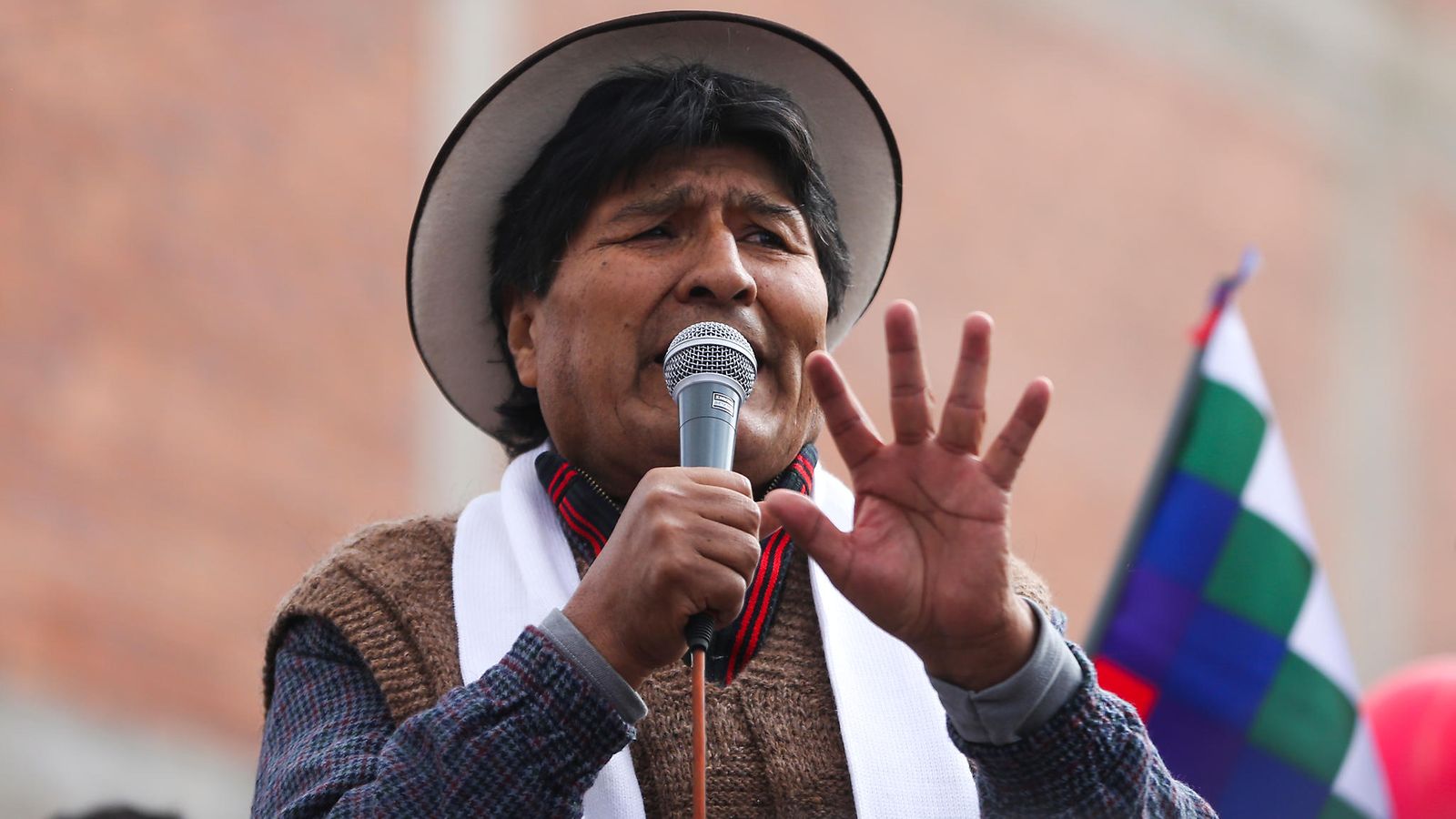 Hattupäinen Evo Morales puhuu mikrofoniin käsi pystyssä.