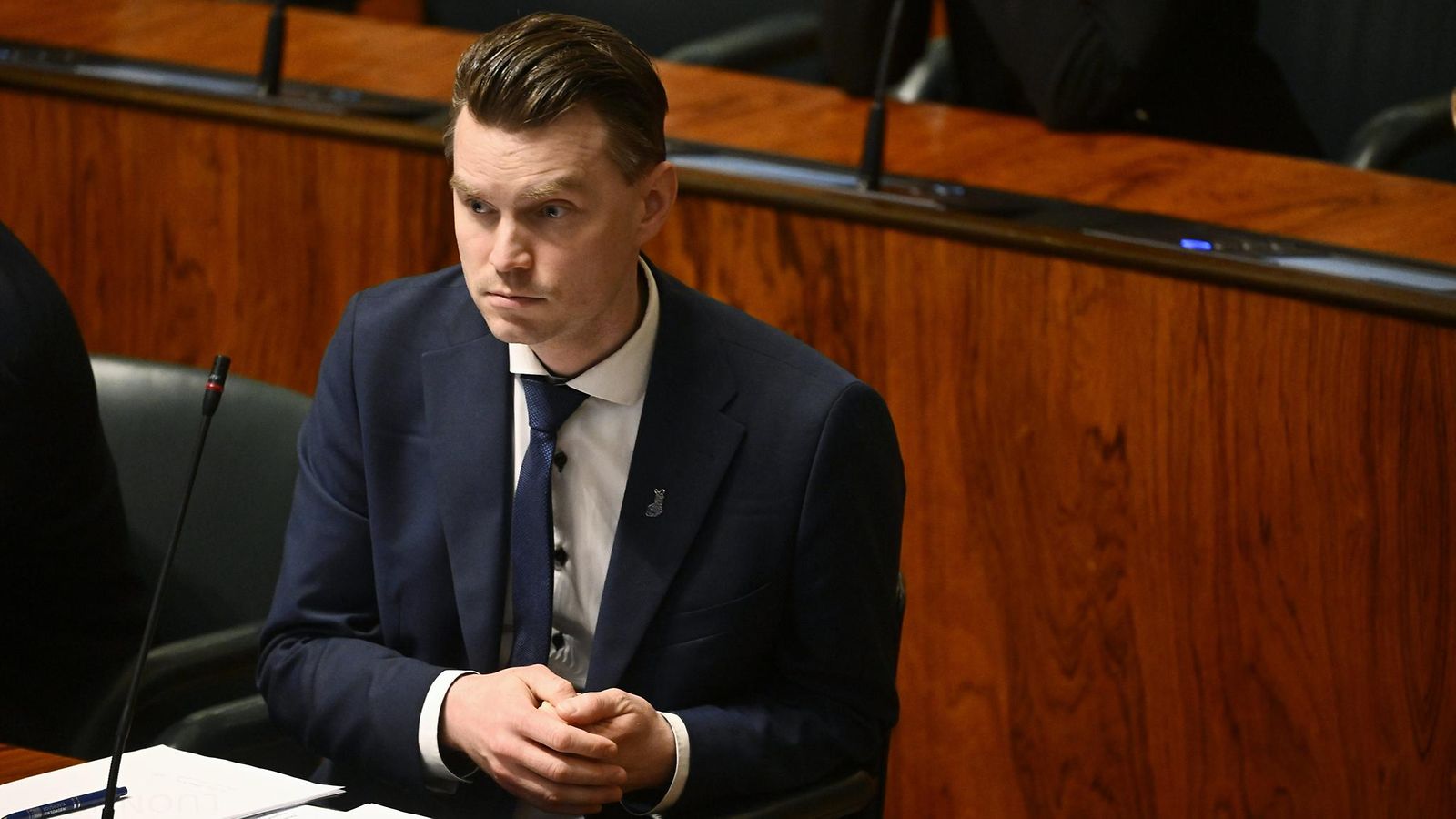 Vakavakatseinen Heikki Autto hieroo käsiään Eduskunnan täysistuntosalissa.