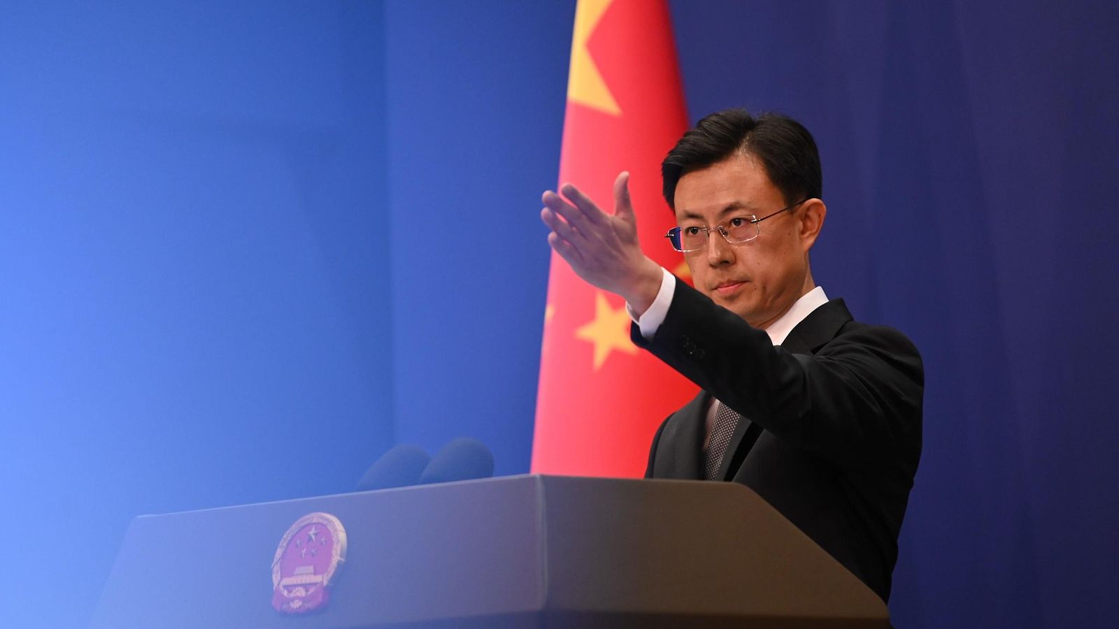 Puhujanpöntön ääressä seisova Guo Jiakun osoittaa kädellä eteenpäin, Kiinan lippu taka-alalla.