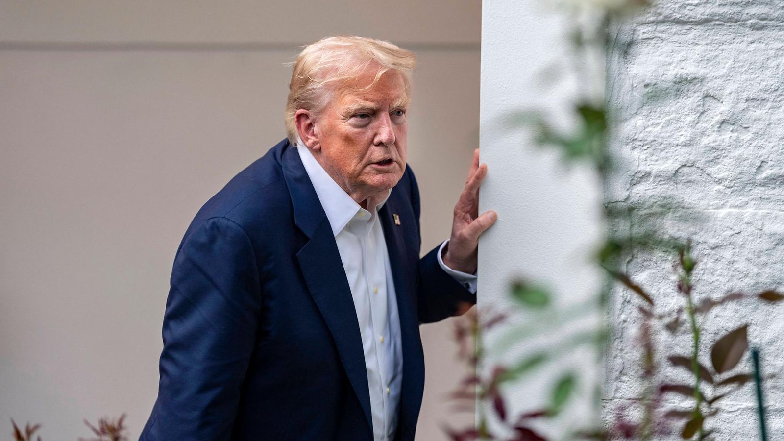 Trump katsoo kysyvästi ottaen samalla tukea Valkoisen talon pylväästä.
