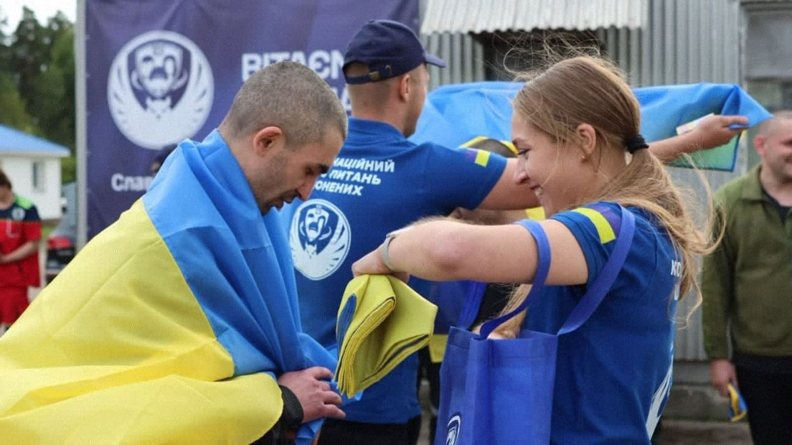 Sotavankien kohtelusta vastaavan koordinaatiokeskuksen 24. elokuuta 2025 julkaisemassa kuvassa työntekijä ojentaa Ukrainan kansallislipun ukrainalaiselle sotavangille vankienvaihdon jälkeen Ukrainassa.