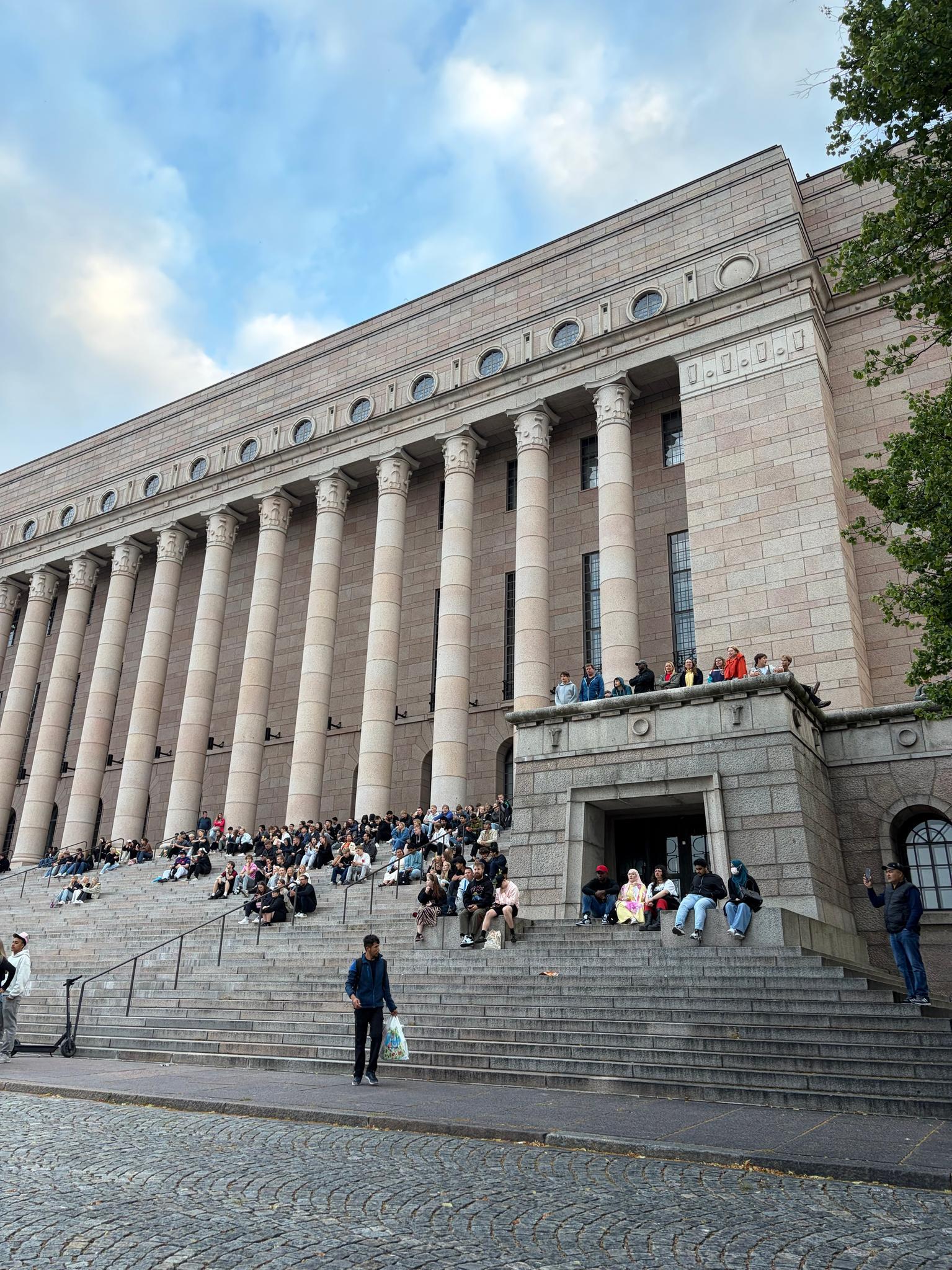Myös Mannerheimintien toisella puolella sijaitsevan Eduskuntatalon portaille on kerääntynyt ihmisiä MM-finaalin alla.
